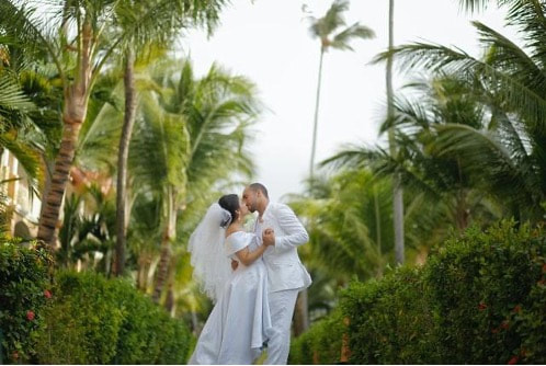 A couple kissing on their wedding day surrounded by palm trees.